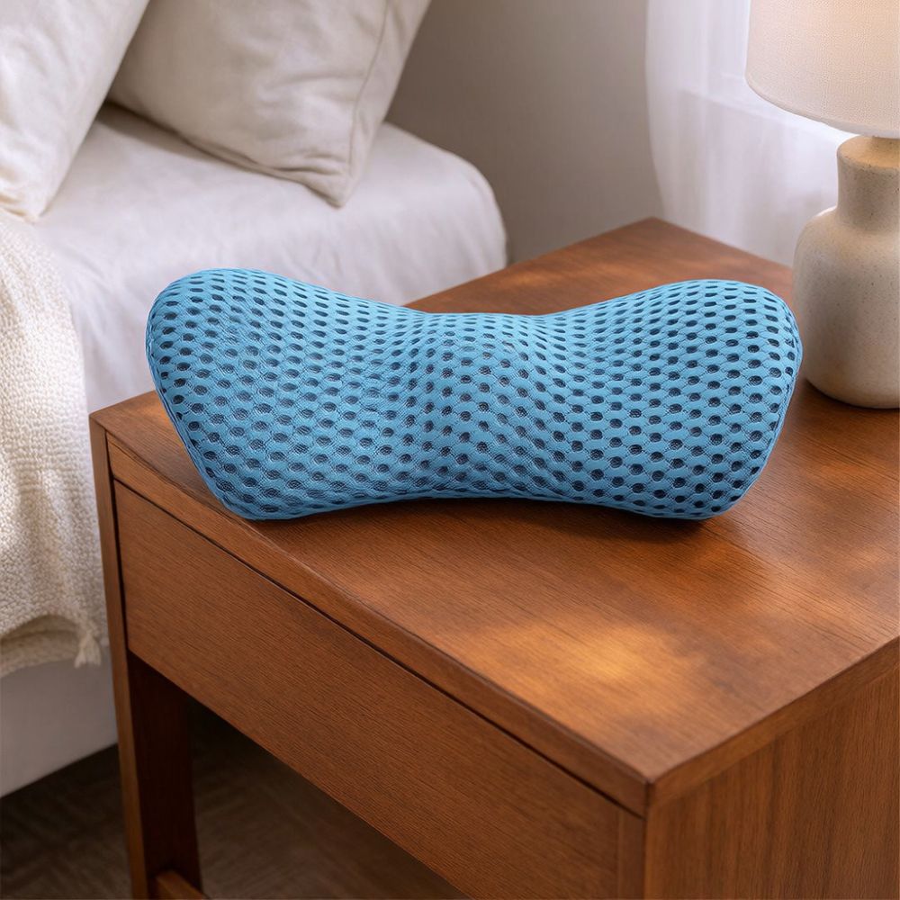 Blue lumbar support pillow with 3D breathable mesh cover resting on a wooden bedside table beside a bed